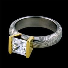 A striking Mokume engagement ring from George Sawyer. The ring features a 5mm grey gold and sterling band. A 1.50ct princess cut diamond is straight V channel set is in warm 18kt yellow gold. Center stone sold separately.